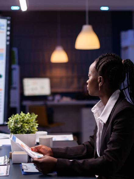 Focused workaholic african american businesswoman working at company financial charts presentation late at night in meeting office room. Overworked manager with dark skin checking profit statistics